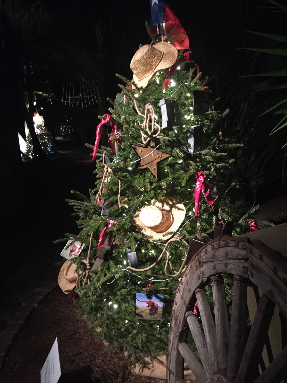 A holiday tree decorated with nautical details beside a wooden wagon wheel.