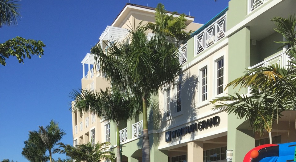 Palm trees against a sunlit pastel hotel building beneath a deep blue sky.