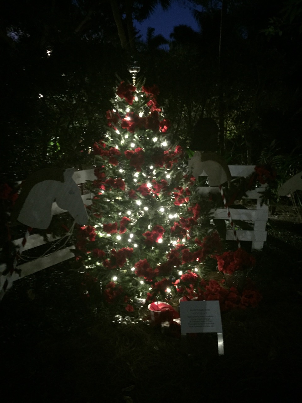 A red-and-white holiday tree glowing beside a garden bench.