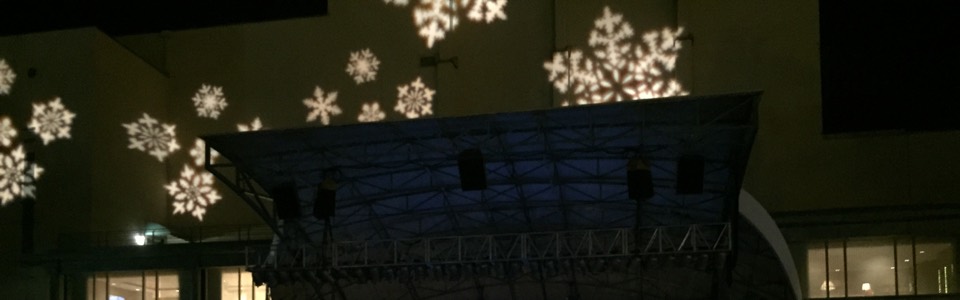 Snowflake light projections above a covered outdoor stage at night.