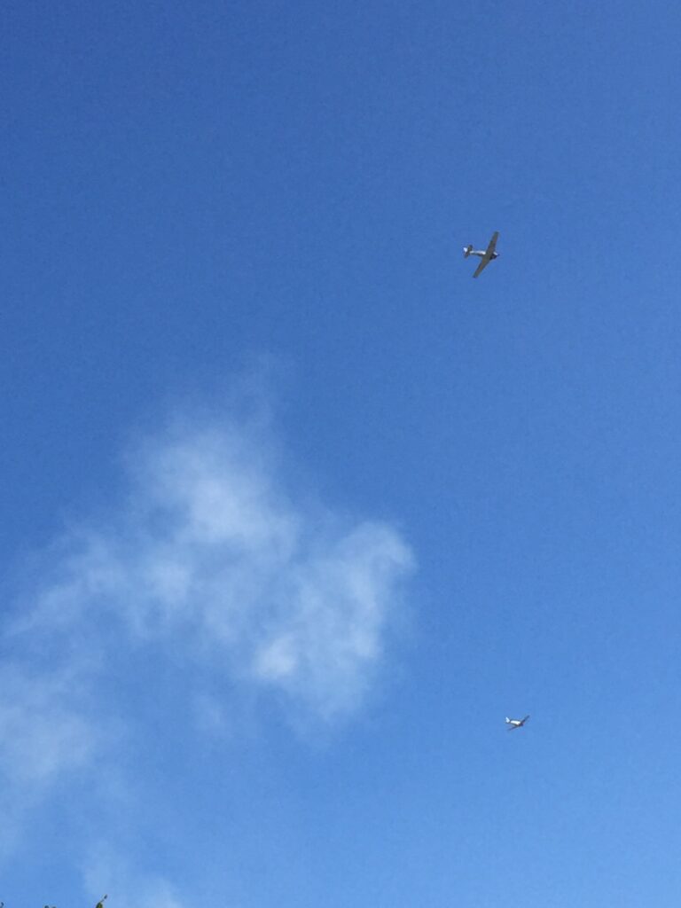 Two small airplanes crossing a blue sky above wispy clouds.