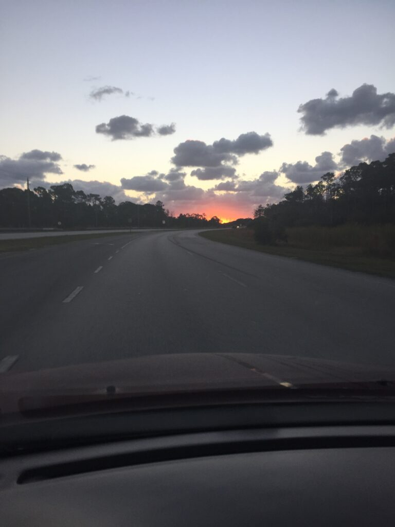 A road beneath scattered clouds and a narrow orange morning horizon.