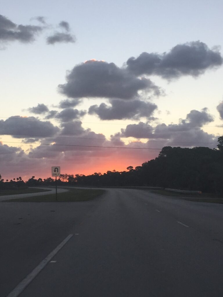 A road beneath gray clouds and an orange morning horizon.