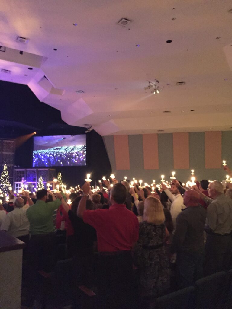 A large indoor gathering holding glowing candles on a December evening.