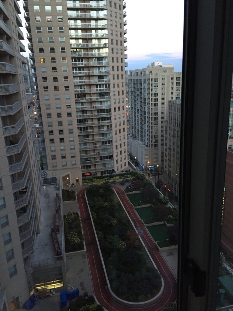 Tall city buildings viewed from a high window at dusk.