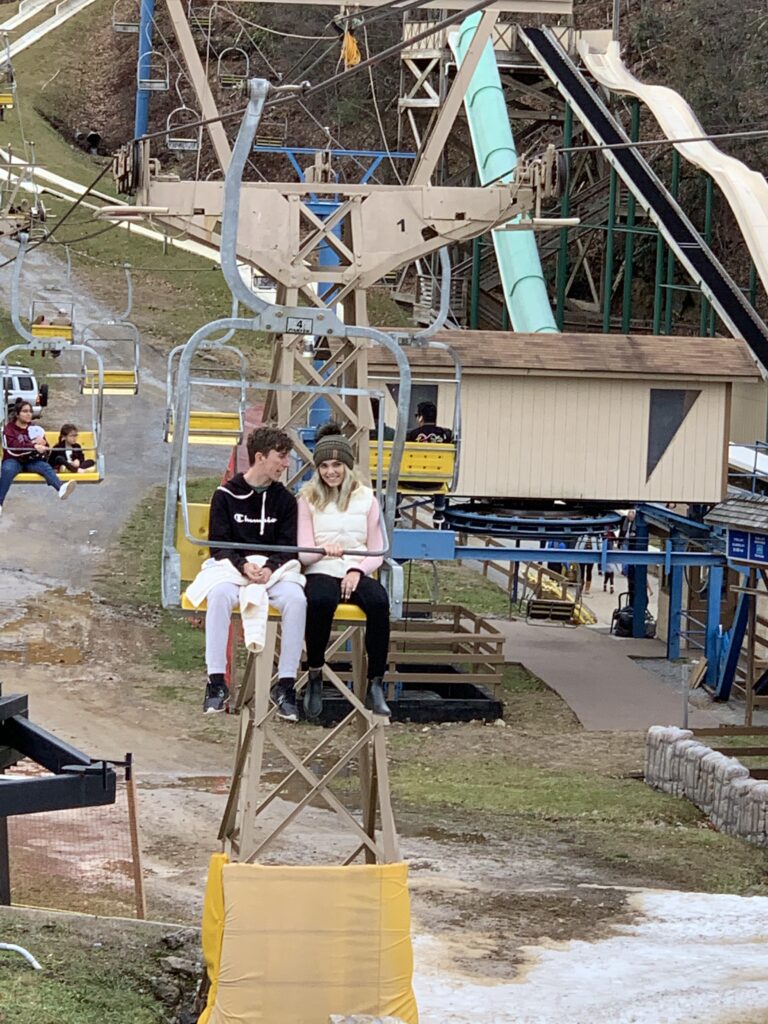 Visitors riding a chairlift above a mountain base.