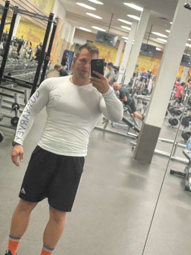 Man in workout clothes taking a gym mirror portrait.