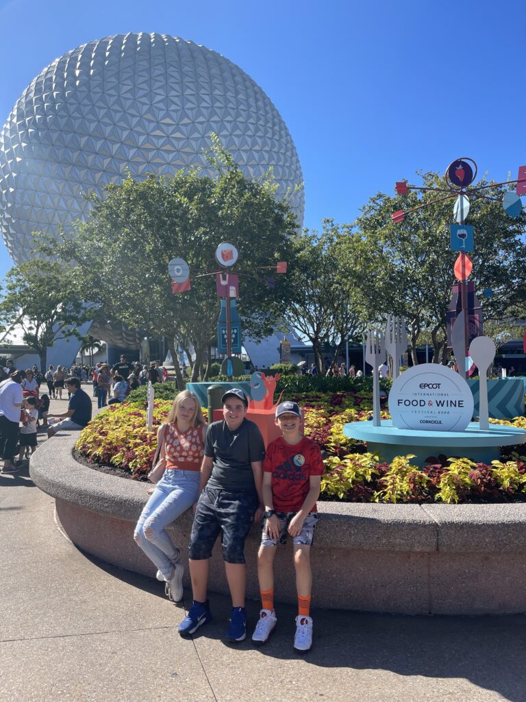 Three children posing in front of Spaceship Earth at EPCOT.