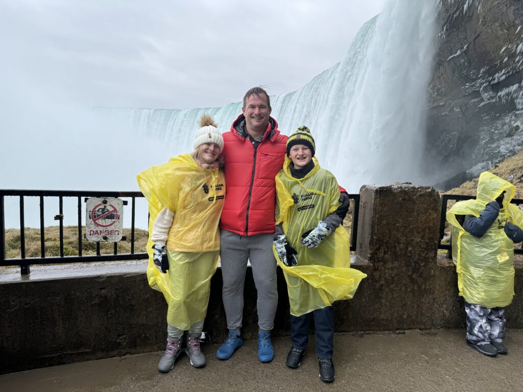 Adult and children in rain ponchos posing beside a waterfall.