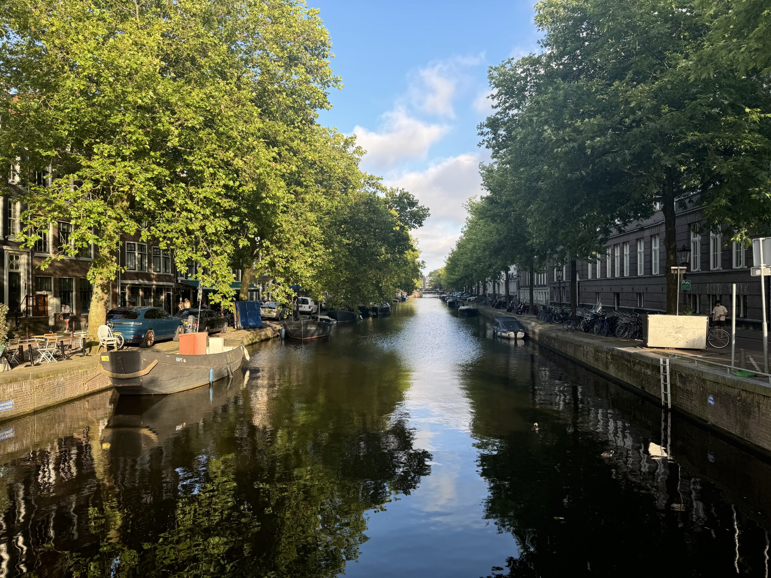 Tree-lined European canal beneath a blue sky.