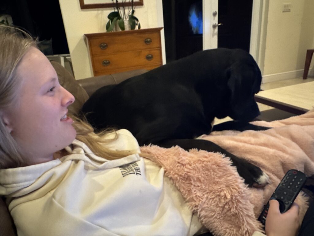 Young person relaxing beside a black dog.