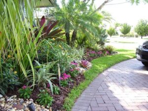 Tropical plants and pink flowers border a curved paved driveway.