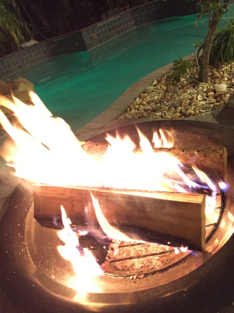 Flames rising from an outdoor fire feature beside a swimming pool at night.