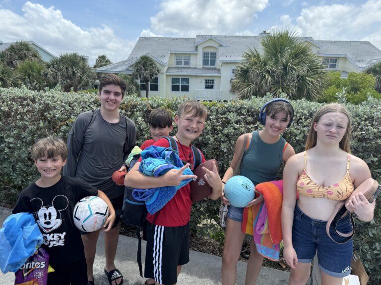 The kids and friends ready for a day outdoors with towels and sports balls.