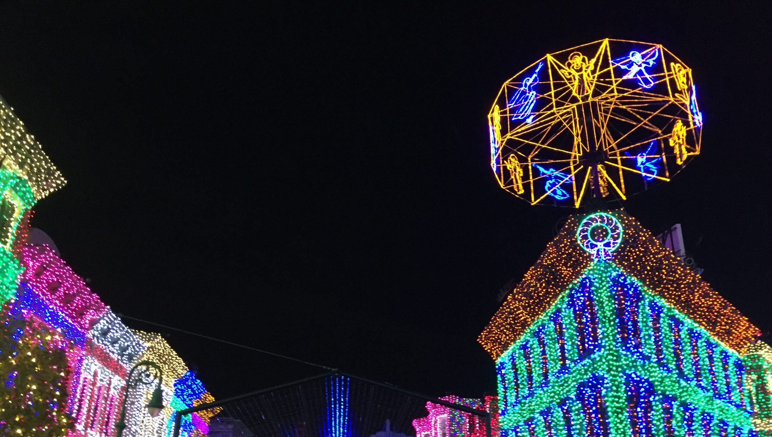 Holiday lights covering buildings beneath a glowing wheel.