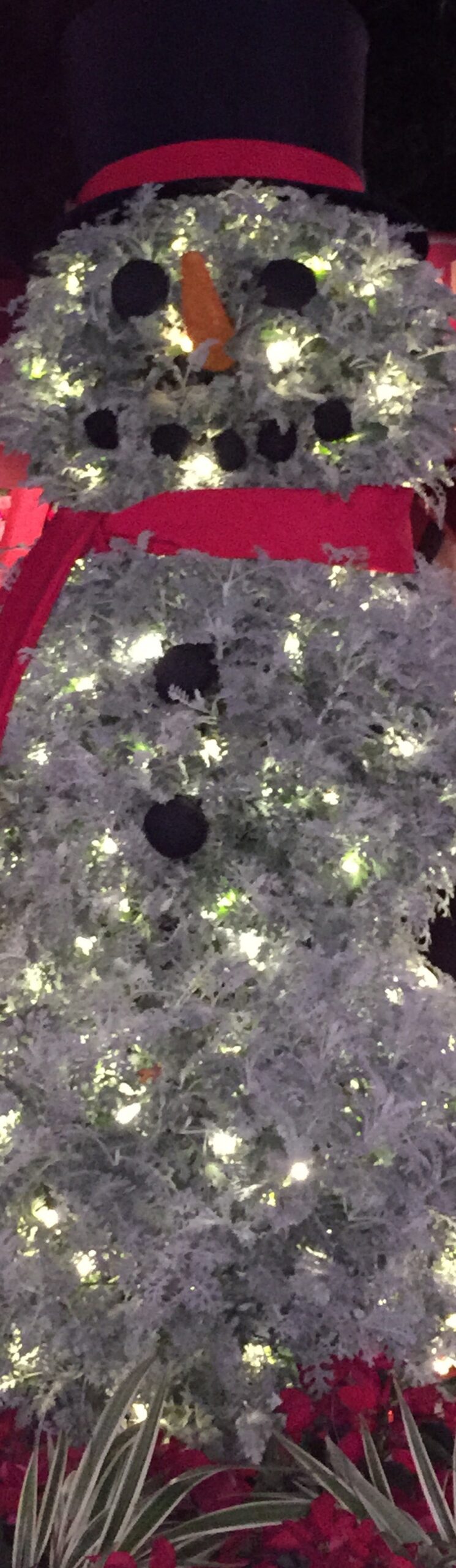 A close detail of a white illuminated snowman with a red scarf and black top hat.
