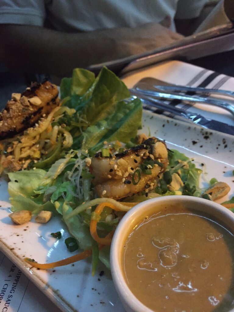 A restaurant plate with noodles, greens, and dipping sauce.