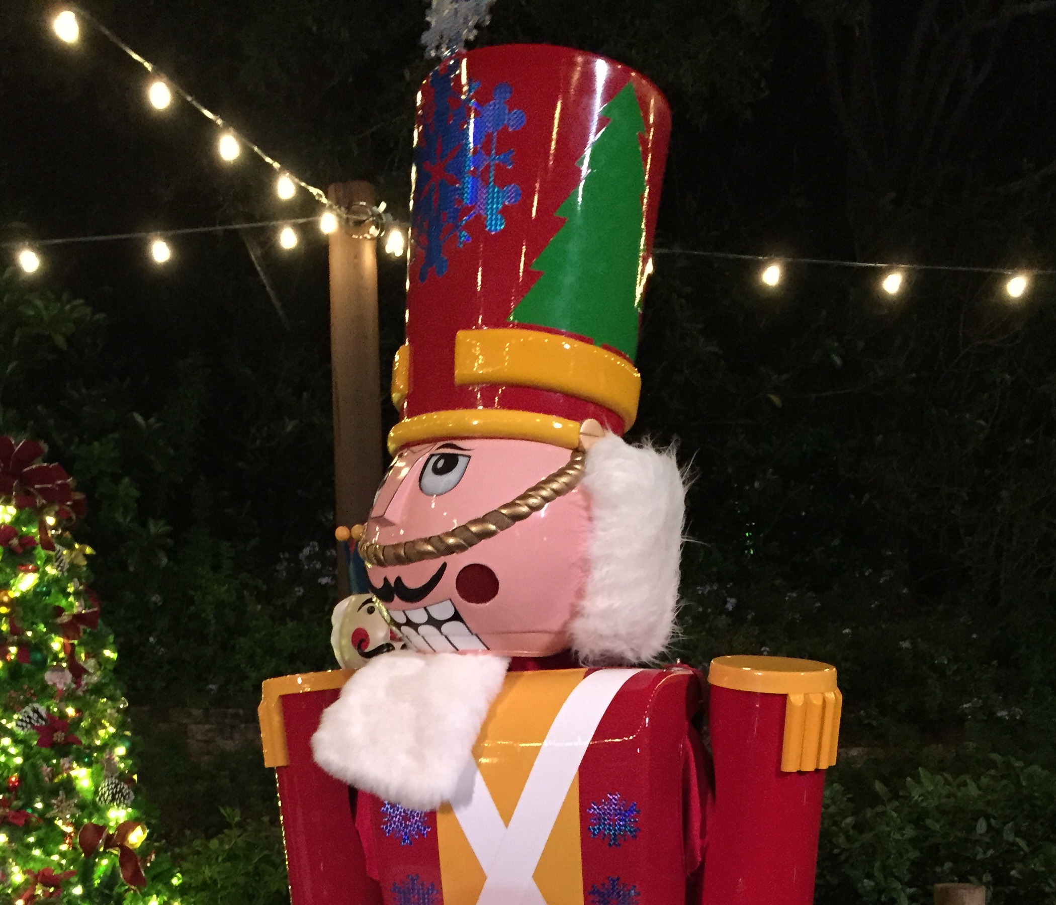 A colorful giant toy soldier beneath glowing string lights at night.