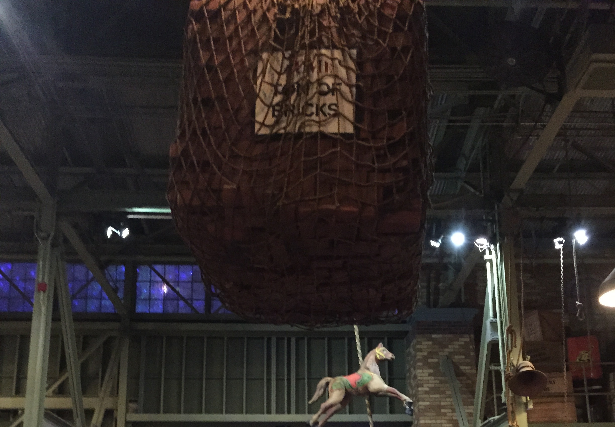 A carousel horse suspended beneath a netted bundle in an indoor display.