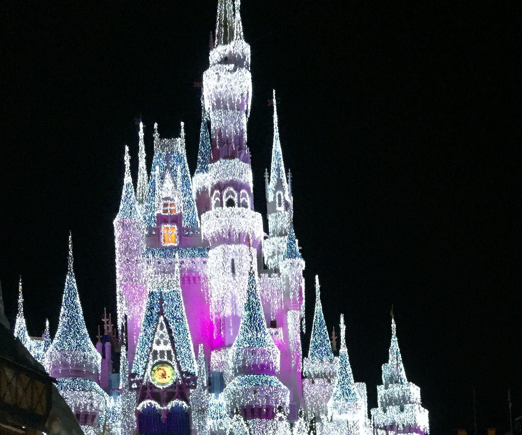 Cinderella Castle sparkling in white, blue, and magenta holiday lights at night.