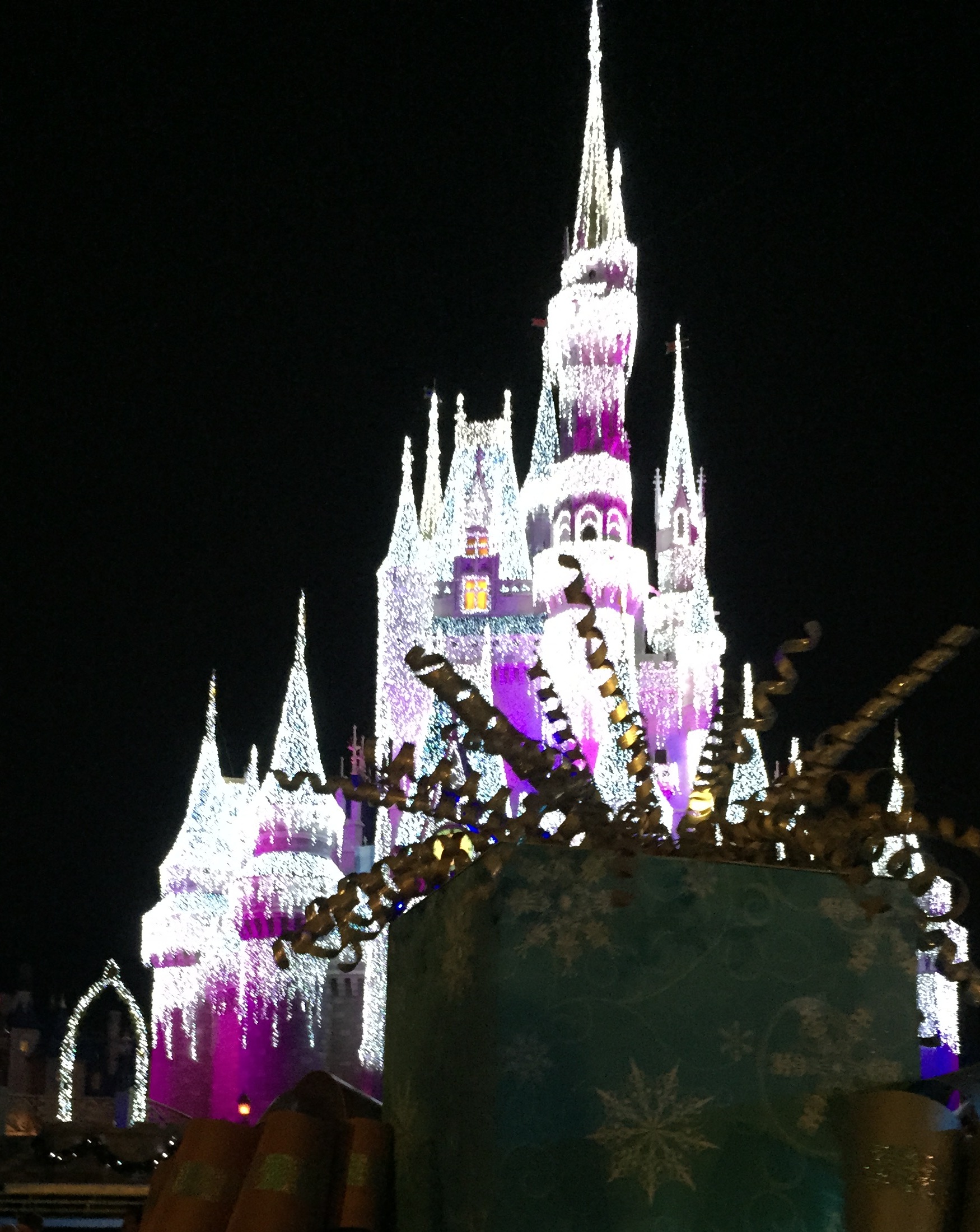 A giant wrapped-present parade float passing in front of Cinderella Castle at night.