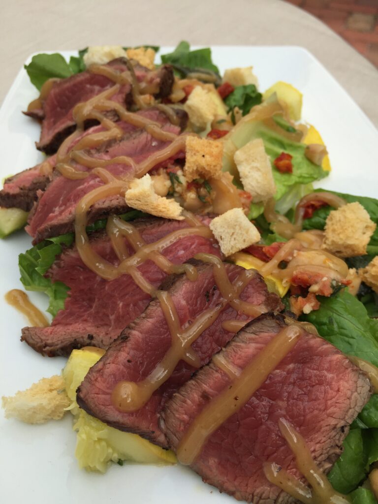Sliced steak over salad greens with croutons and dressing.