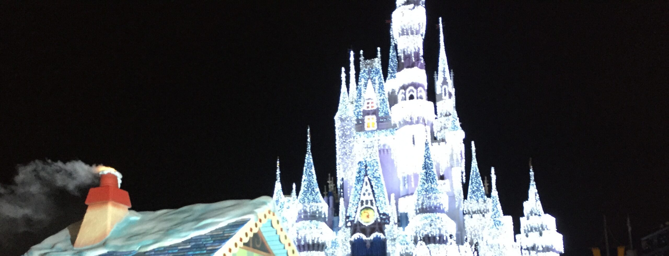Snow-covered parade rooftop passing beneath the illuminated Cinderella Castle at night.