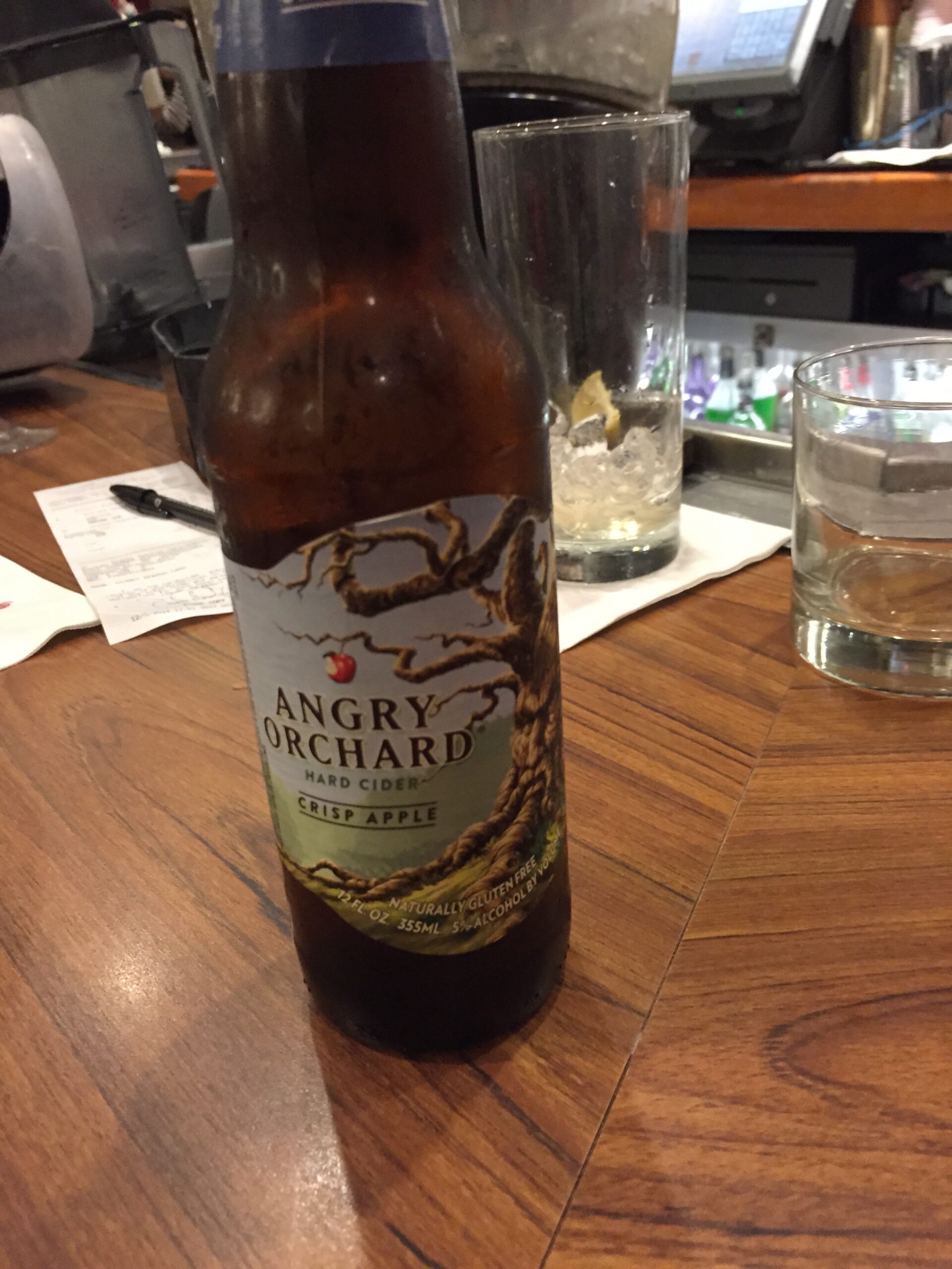 Bottle of Angry Orchard hard cider on a restaurant table beside glasses of water.