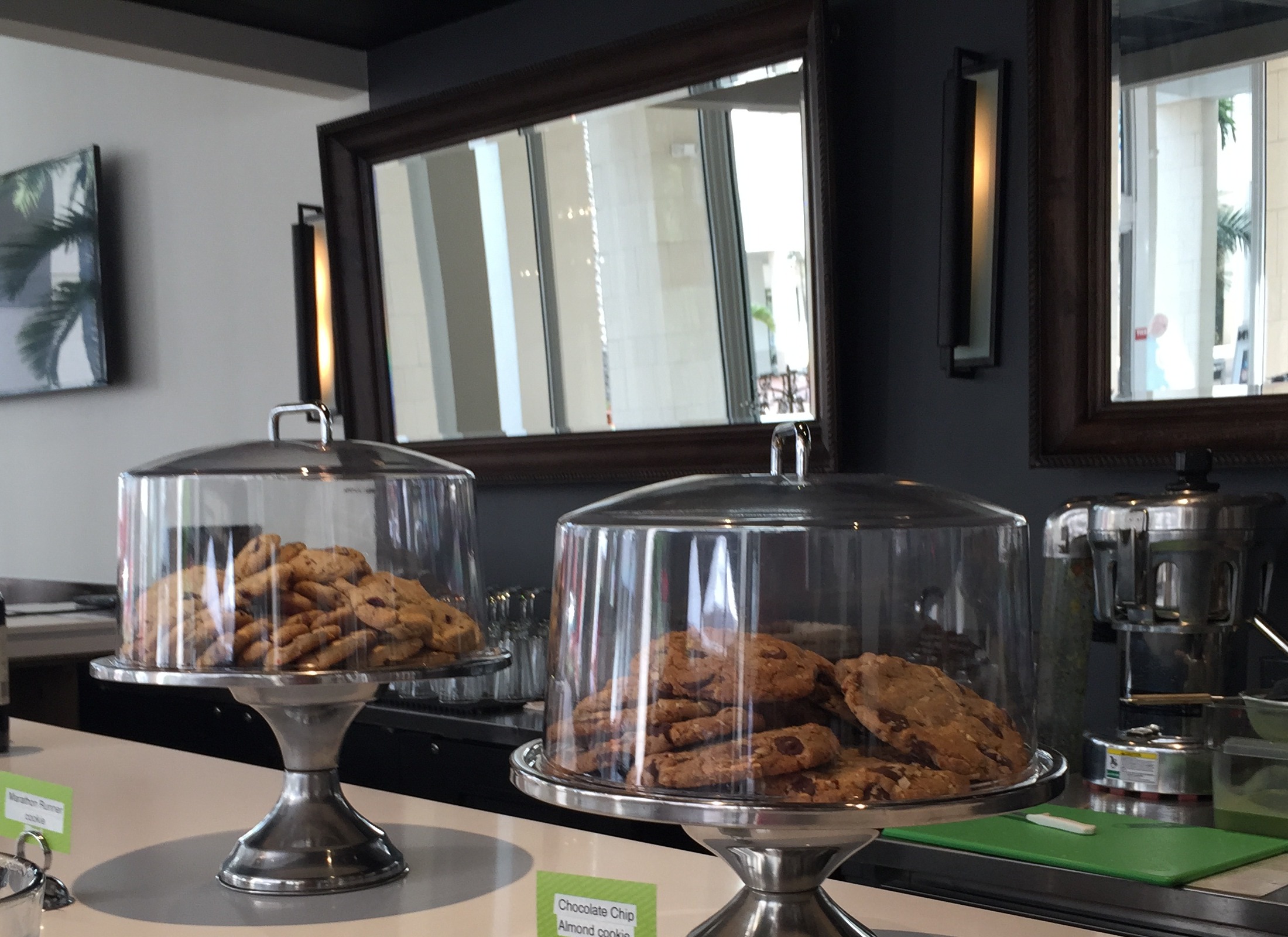 Cookies displayed under glass domes beside wine bottles at a cafe counter.
