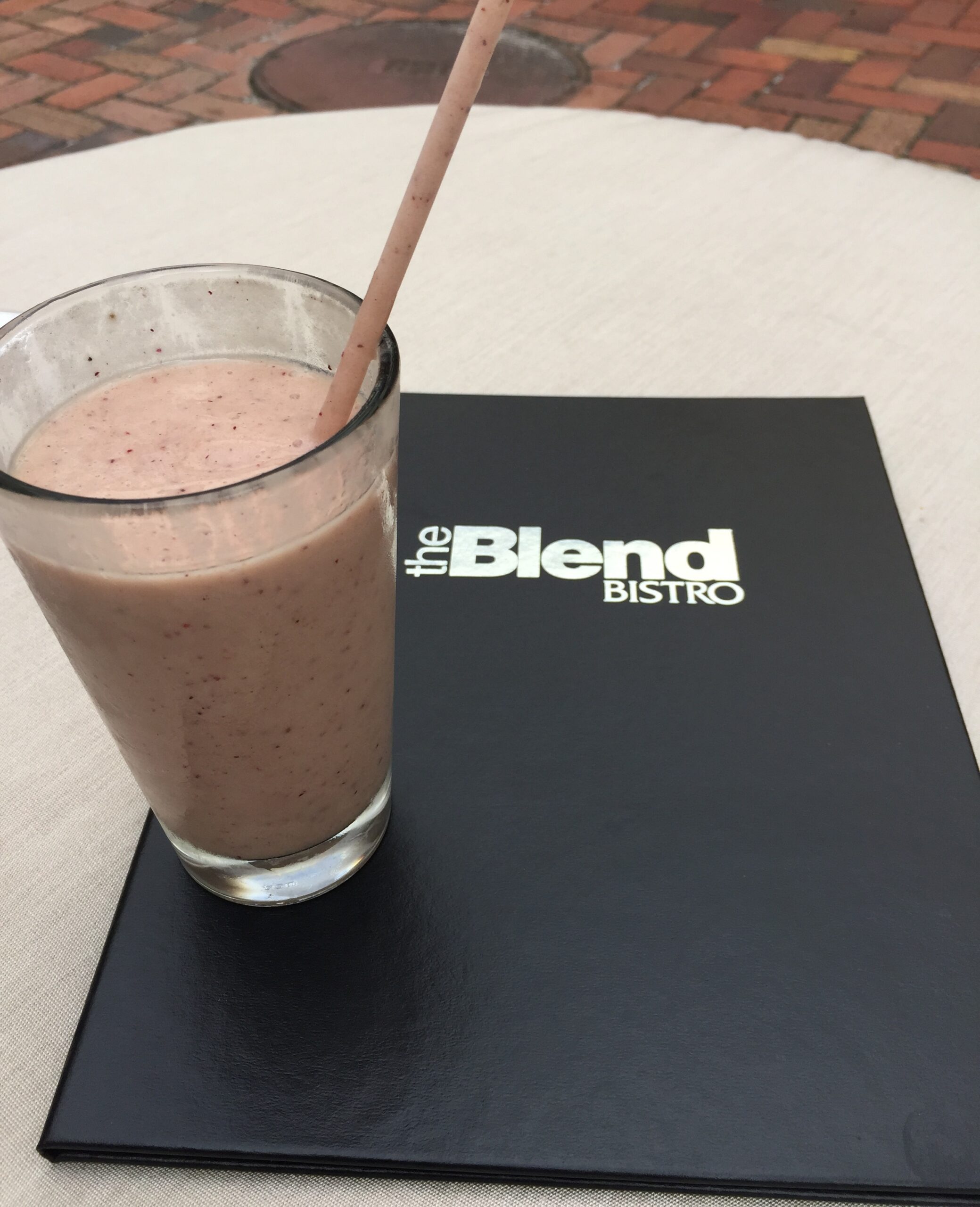 Berry-colored smoothie beside a black The Blend Bistro menu on a white table.