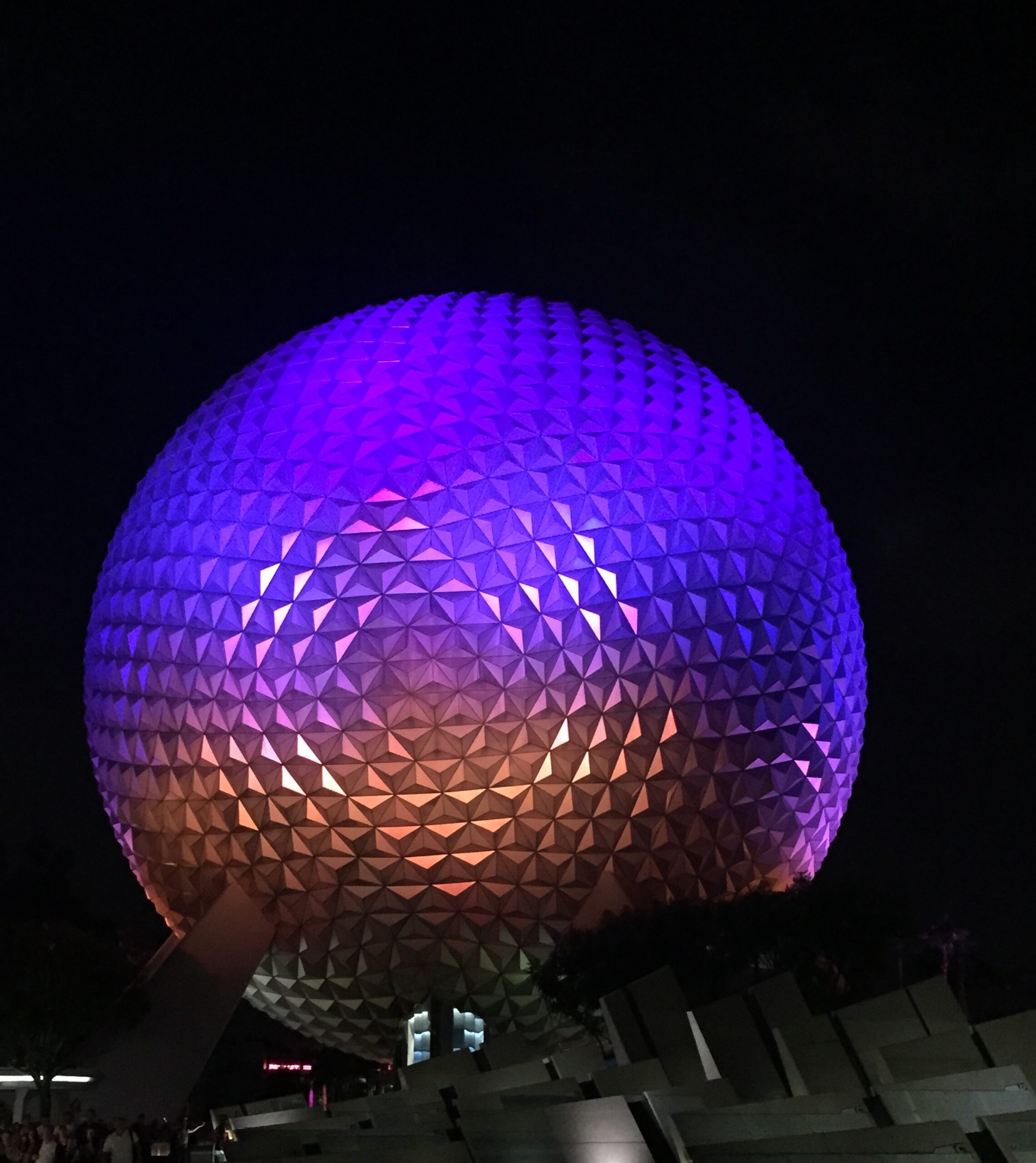 Spaceship Earth illuminated in purple and amber against the night sky.