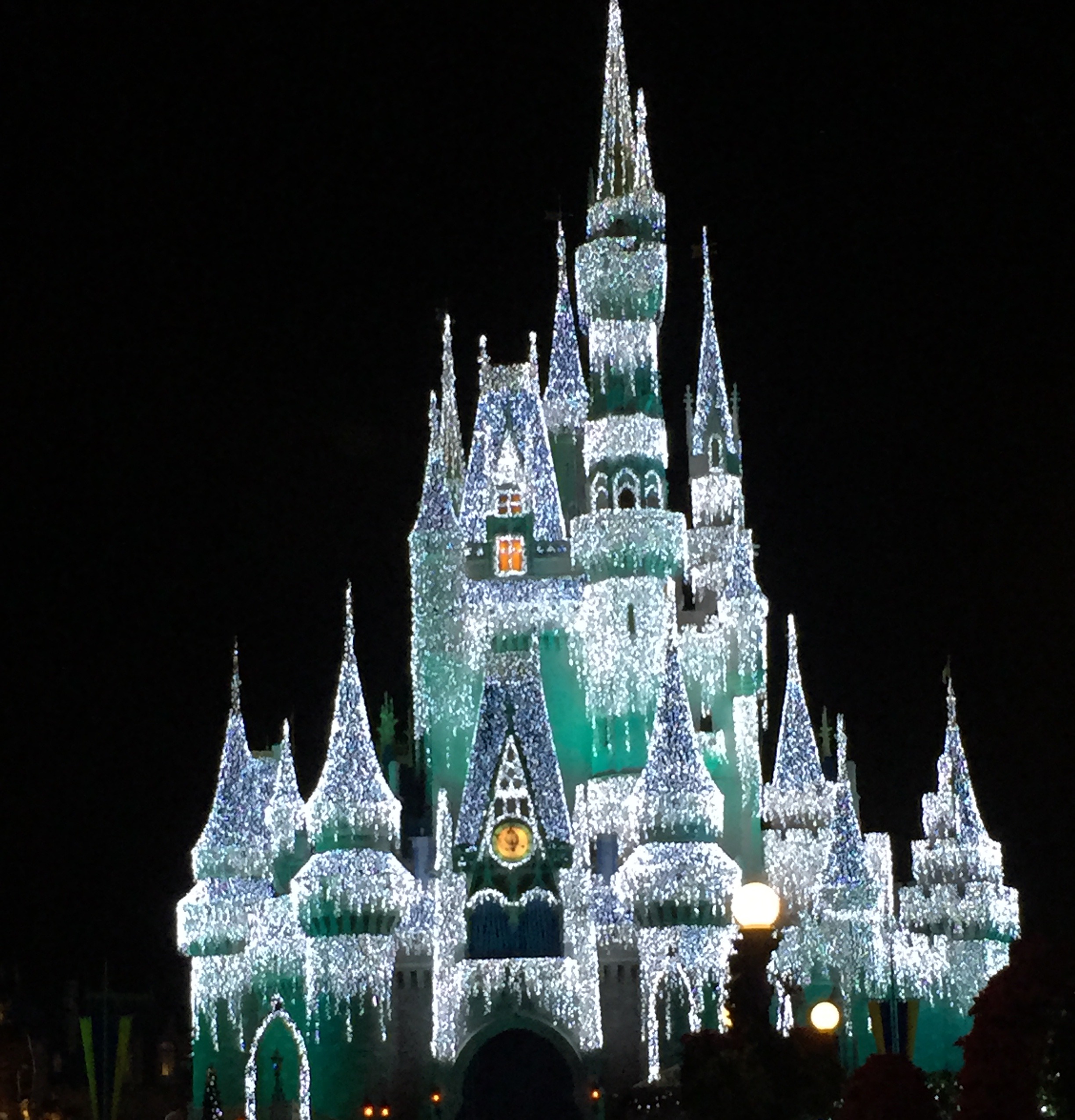 Cinderella Castle illuminated in icy white and green holiday lights at night.