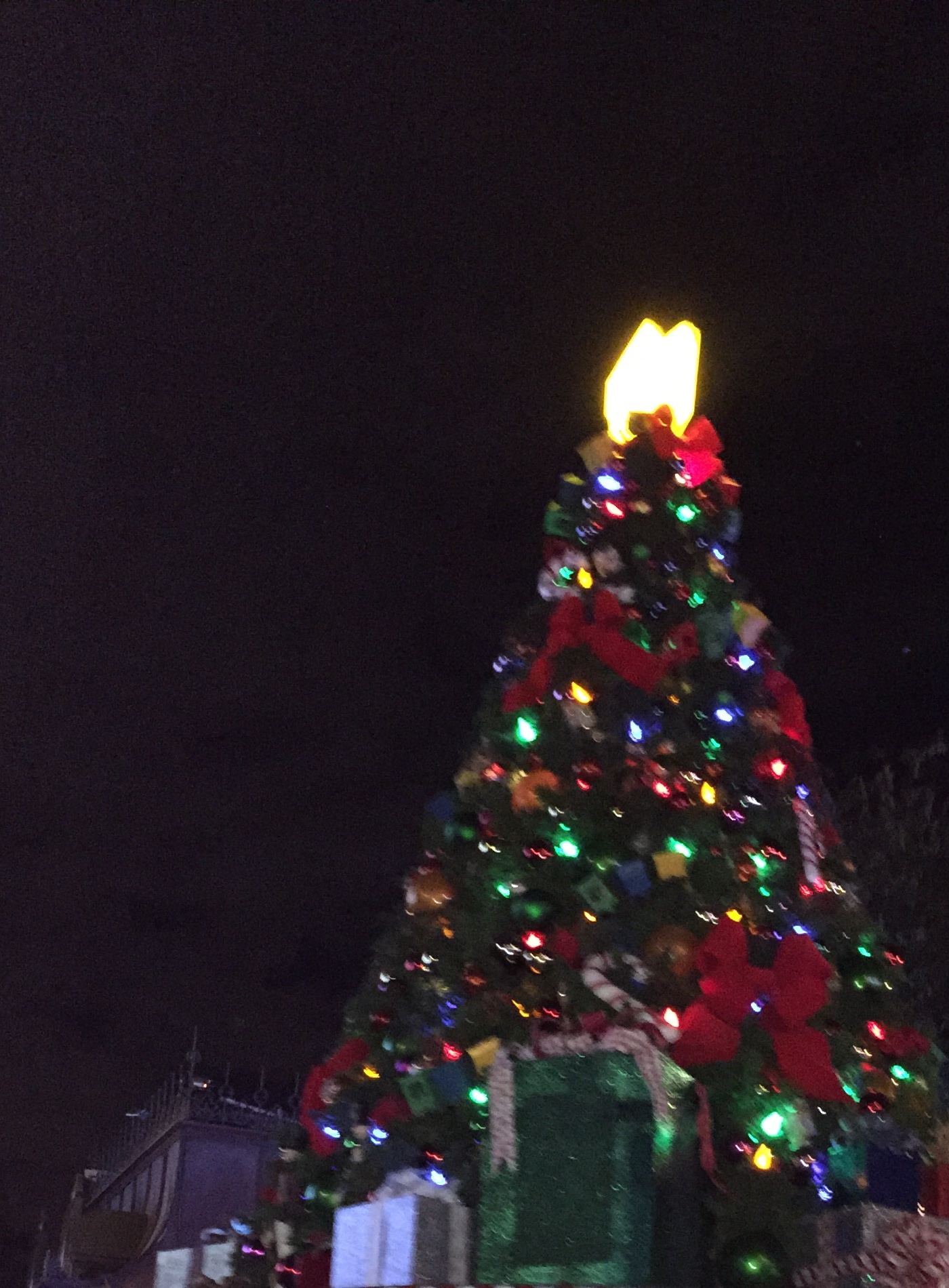 An illuminated Christmas-tree parade float decorated with gifts, ribbons, and multicolored lights.