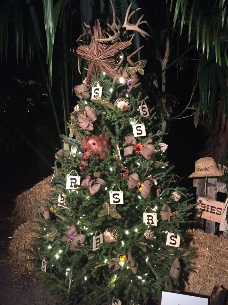 A rustic decorated holiday tree lit outdoors at night.
