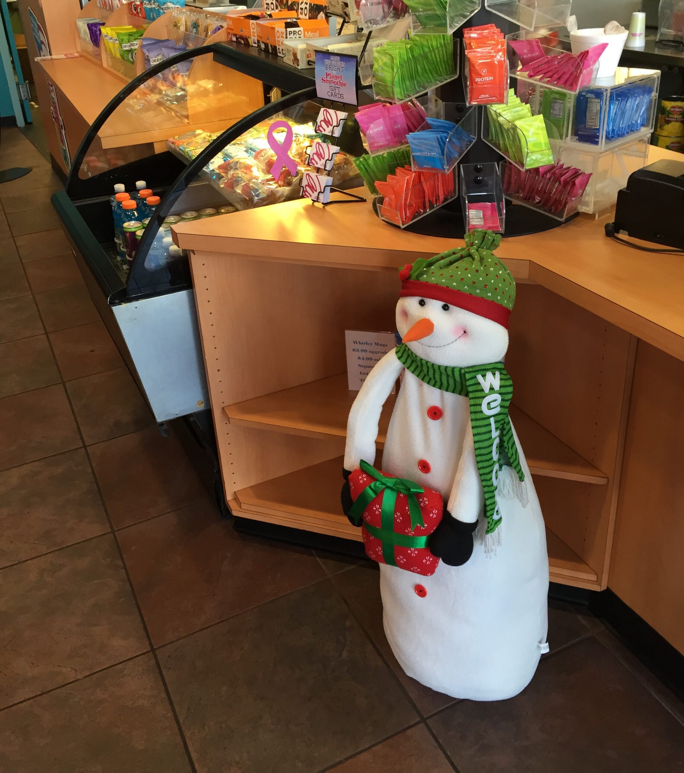 A plush holiday snowman holding a wrapped present beside a smoothie-shop counter.